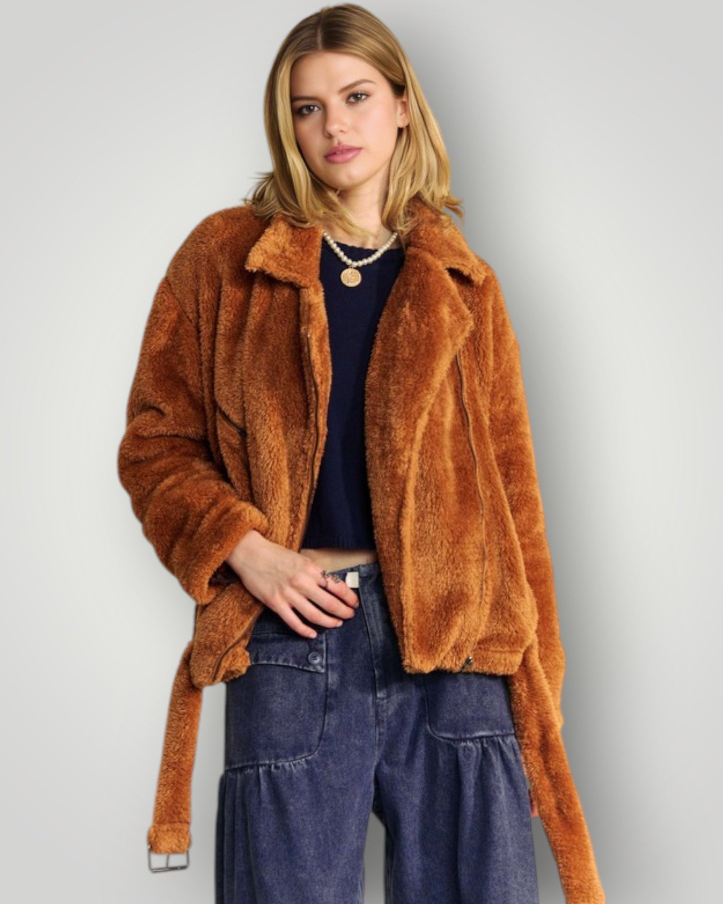 Woman wearing a brown fuzzy jacket and blue jeans on a plain background