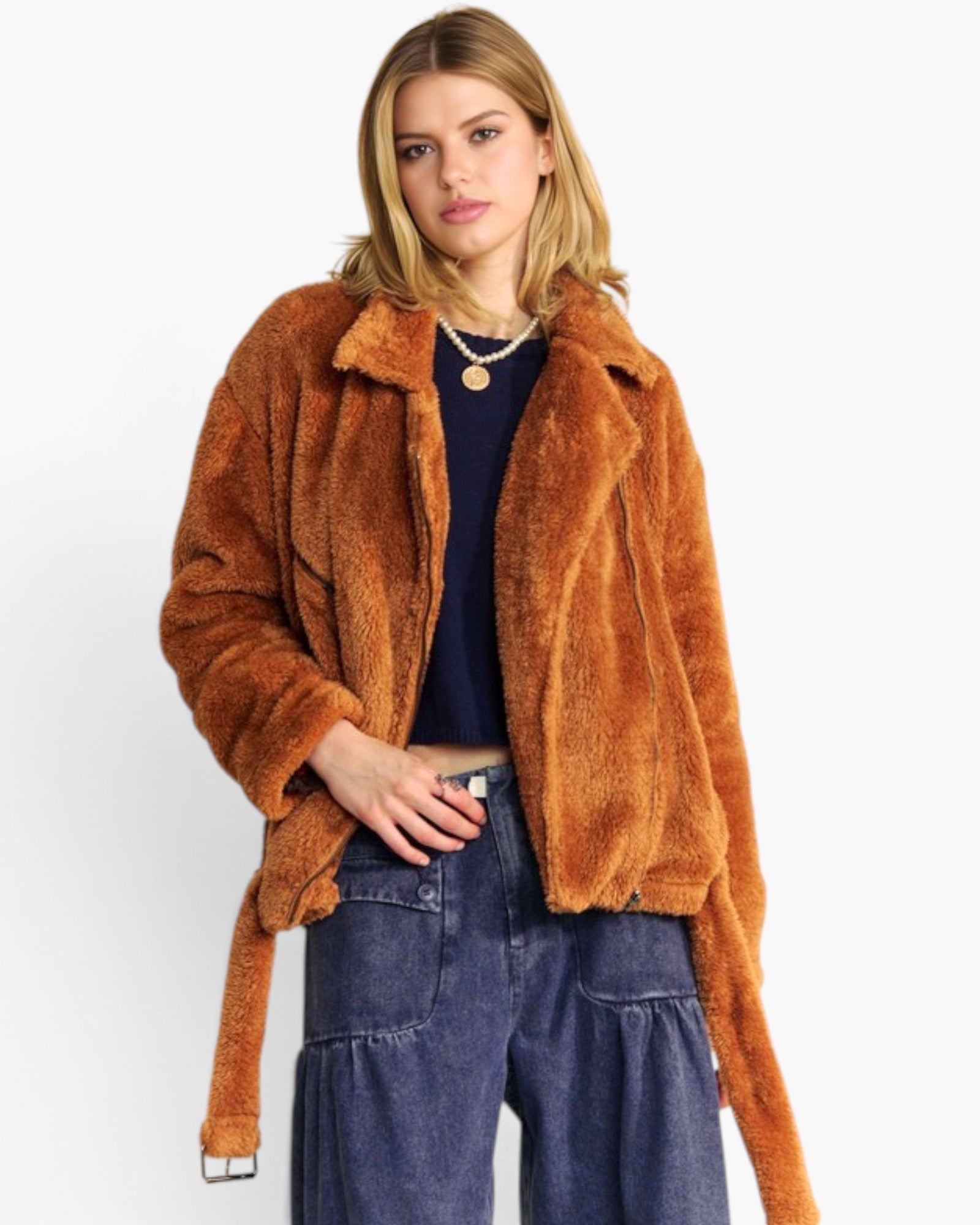 A woman modeling a brown faux fur jacket with a tie belt, worn over a navy top and blue jeans, against a plain white background.