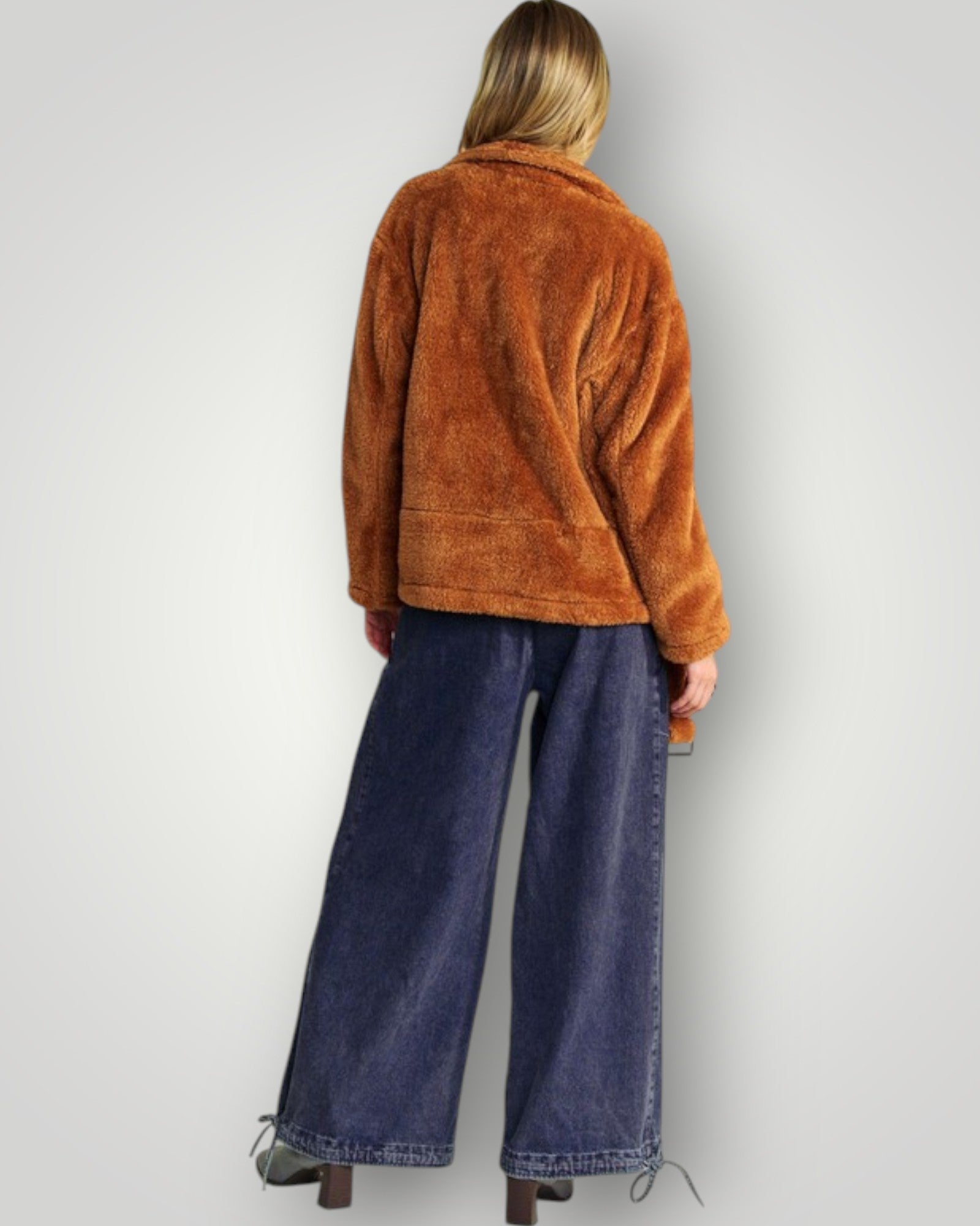 Person wearing a brown jacket and blue jeans against a white background