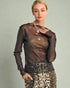 Woman wearing a sheer black top and leopard print pants against a plain background