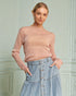 Woman wearing a pink sweater and denim skirt against a light green wall.