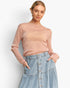 A woman modeling a long-sleeve, semi-sheer knit top in a dusty rose pink color, paired with a light blue denim skirt, against a plain white studio background.