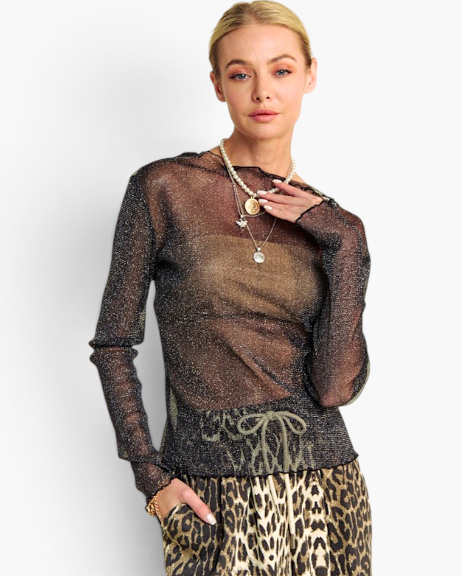 A blonde model wearing a sheer, sparkly brown long-sleeve top with a drawstring waist, paired with a leopard print skirt, against a plain light gray background.