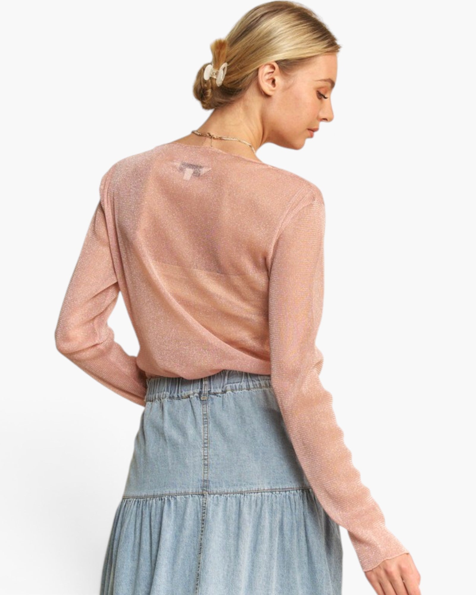 A woman shown from the back wearing a shimmering dusty pink long-sleeve knit top and a light blue denim skirt against a plain white background.