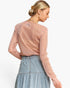 A woman shown from the back wearing a shimmering dusty pink long-sleeve knit top and a light blue denim skirt against a plain white background.