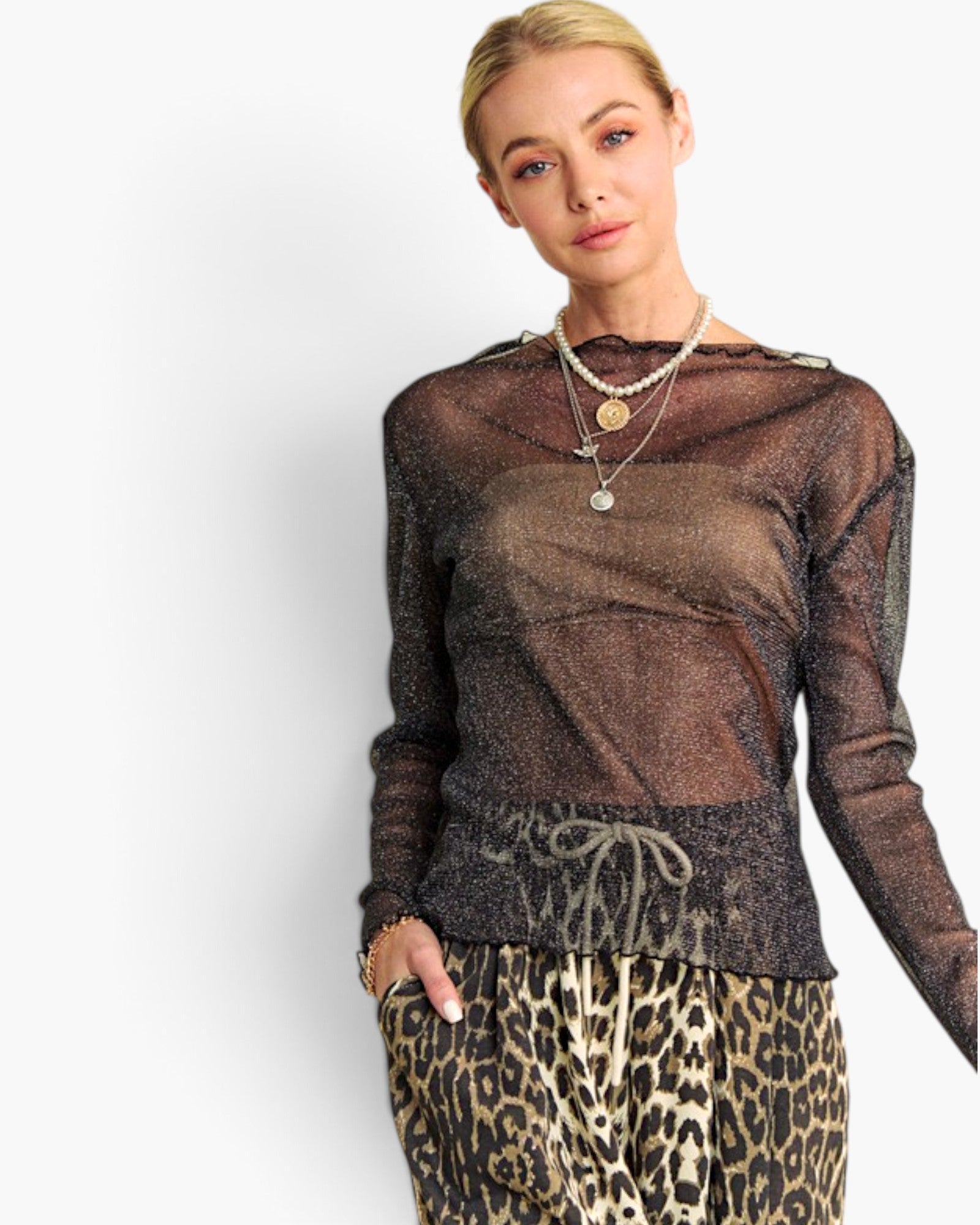 A woman modeling a sheer, long-sleeve metallic mesh top in a bronze-brown color, paired with leopard-print pants and layered necklaces, against a plain white background.