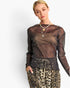 A woman modeling a sheer, long-sleeve metallic mesh top in a bronze-brown color, paired with leopard-print pants and layered necklaces, against a plain white background.