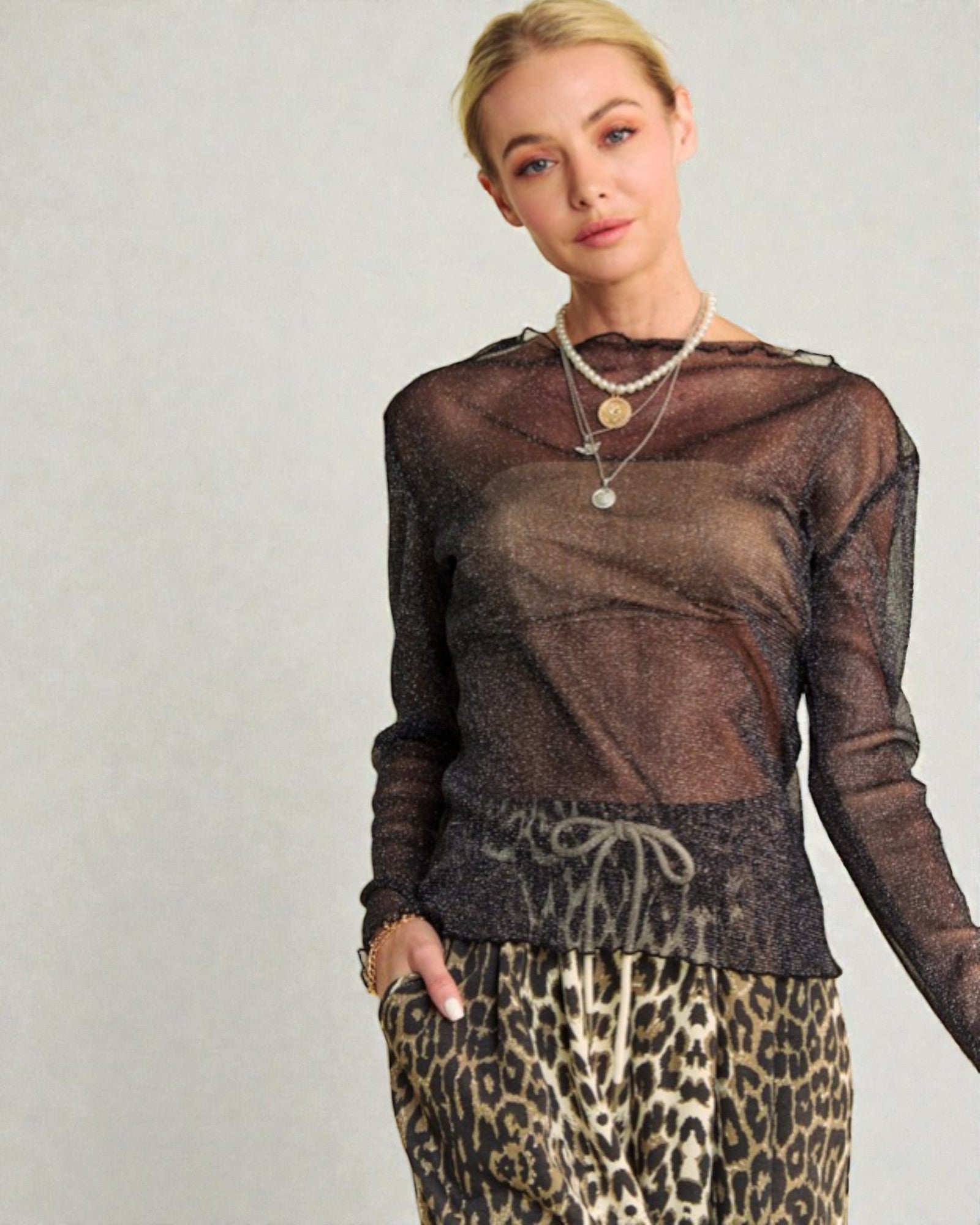 Woman wearing a sheer brown top and leopard print pants against a plain background