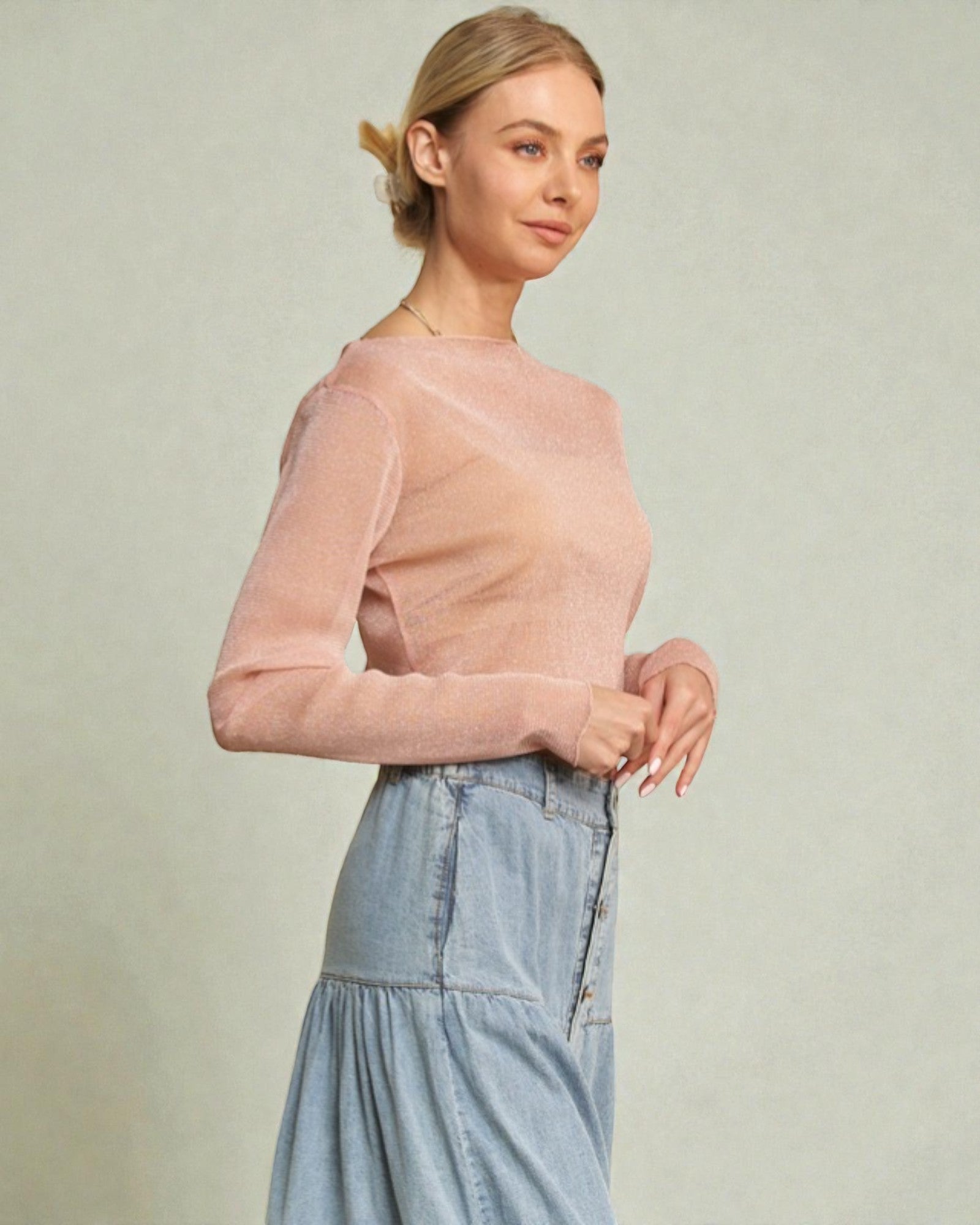 Woman wearing a pink sweater and light blue denim skirt on a plain background