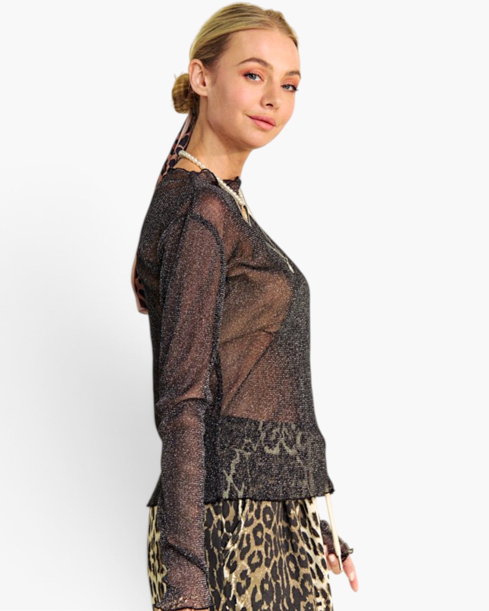 A woman wearing a sheer black long-sleeve mesh top with a subtle glittery texture and leopard-print bottoms, photographed against a clean white studio background.