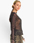 A woman wearing a sheer black long-sleeve mesh top with a subtle glittery texture and leopard-print bottoms, photographed against a clean white studio background.