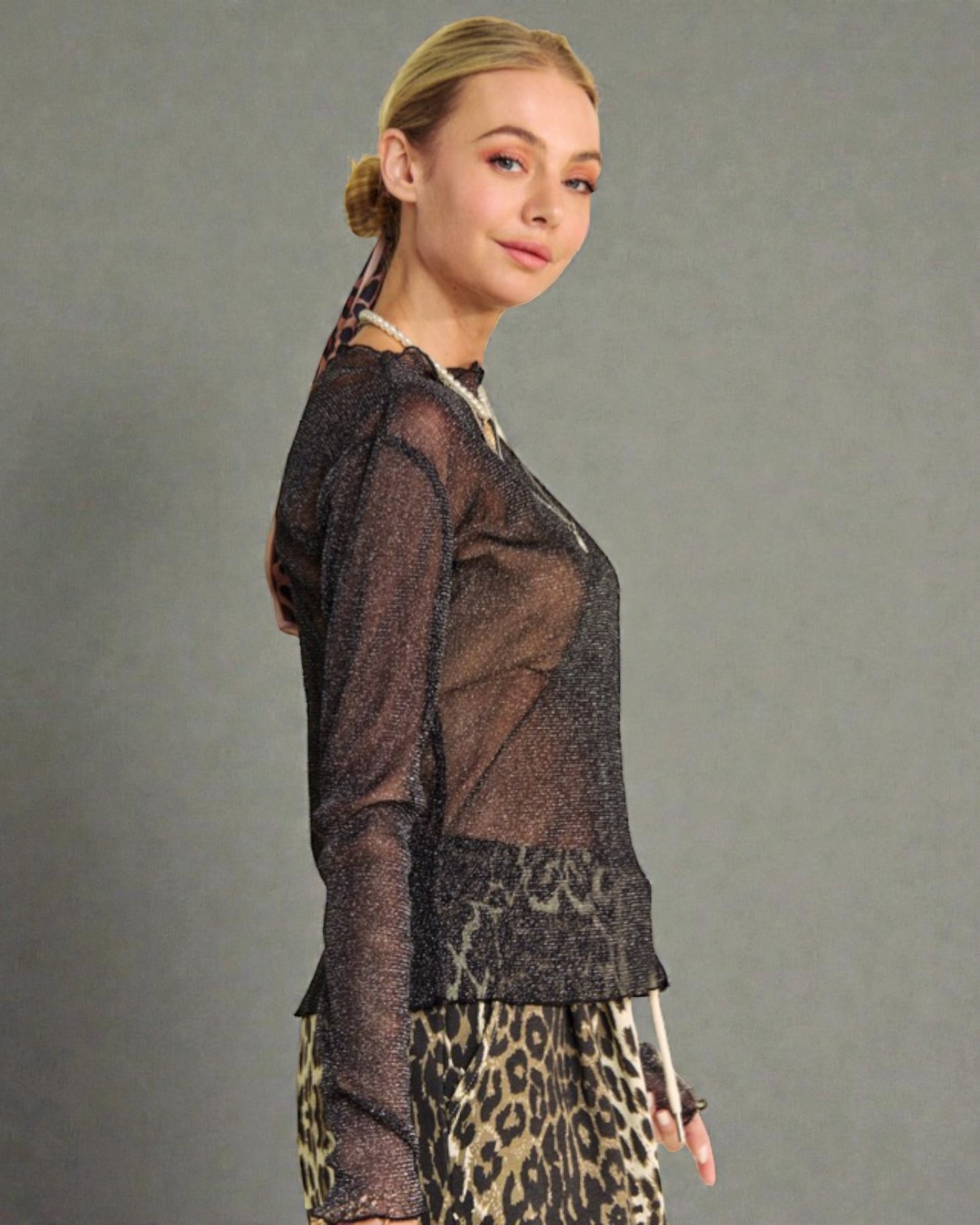 Woman wearing a sheer black top and leopard print pants against a gray background