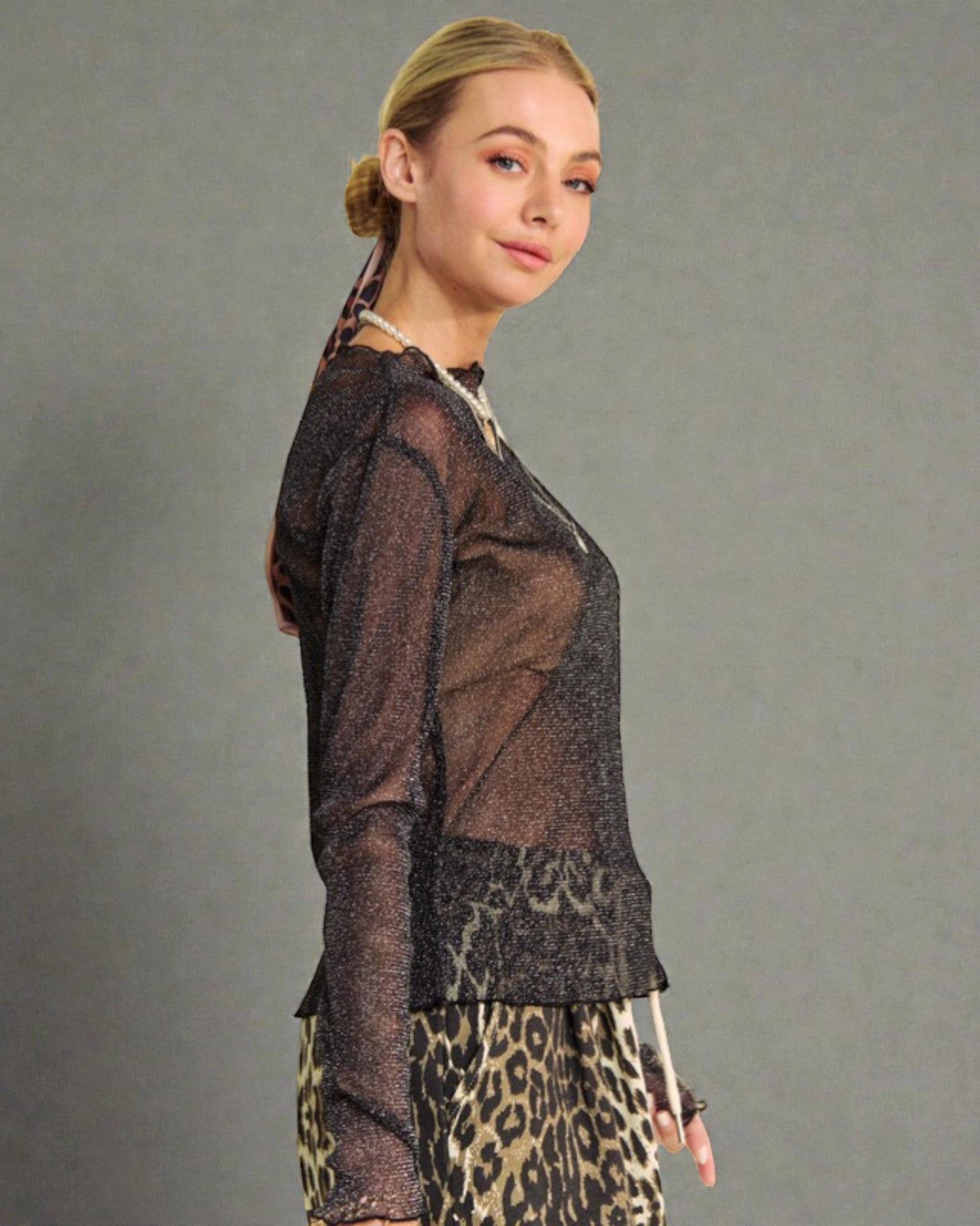 Woman wearing a sheer black top and leopard print pants against a gray background