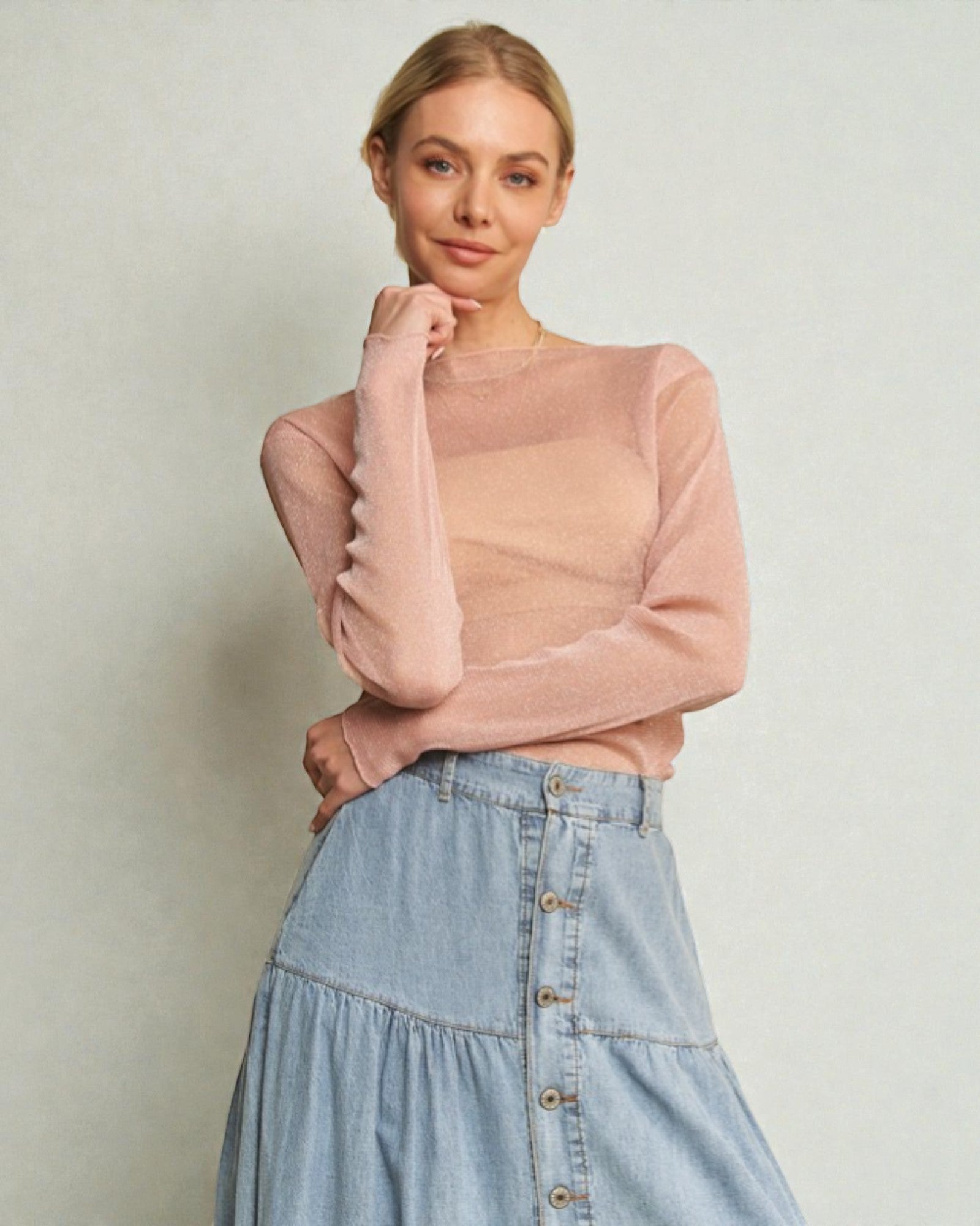 Woman wearing a pink sweater and denim skirt against a plain background
