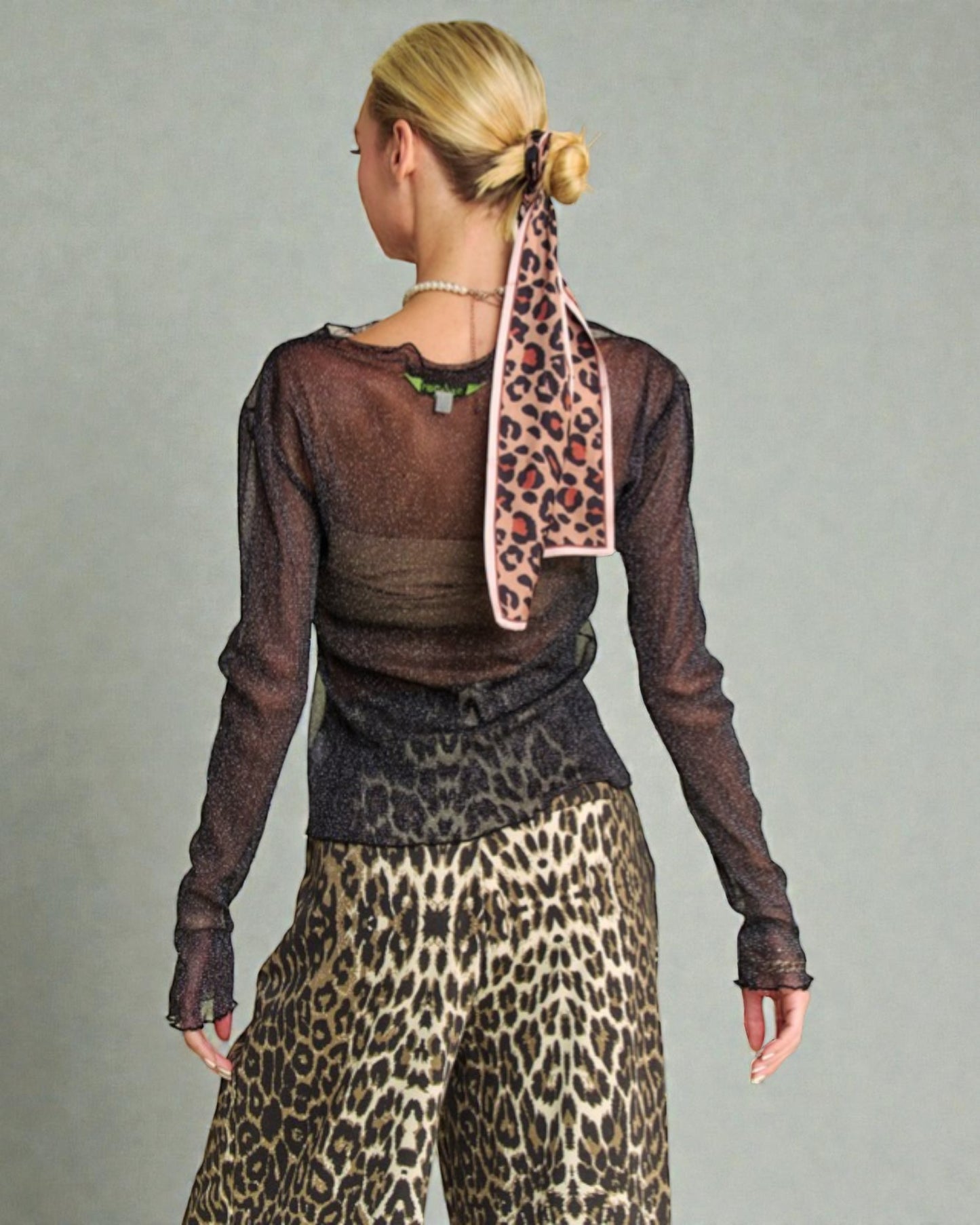 Person wearing a sheer brown top and leopard print pants with a matching scarf on a gray background