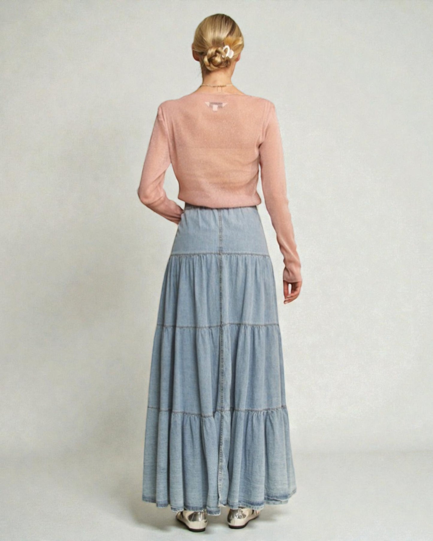 Woman wearing a pink top and blue tiered skirt on a plain background