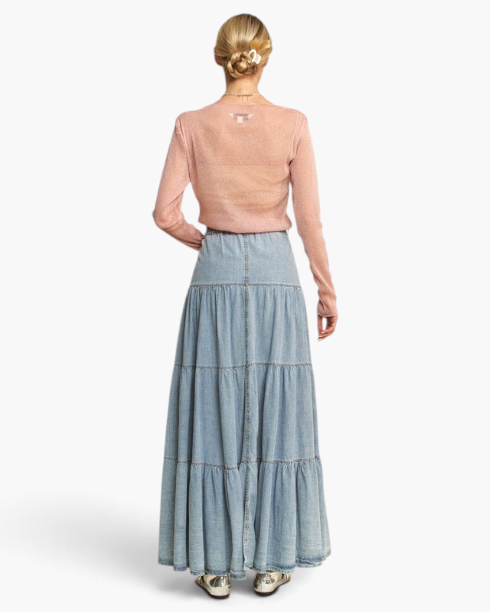 A model shown from the back wearing a light pink long-sleeve knit top and a light blue denim tiered maxi skirt, set against a plain white studio background.