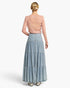A model shown from the back wearing a light pink long-sleeve knit top and a light blue denim tiered maxi skirt, set against a plain white studio background.