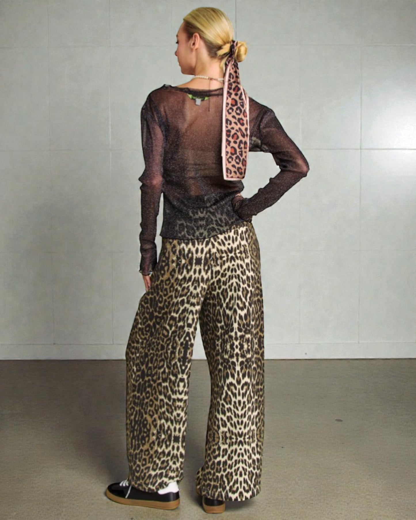Person wearing a sheer top and leopard print pants with a matching scarf against a plain background