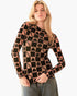 A woman modeling a long-sleeve knit top with a black and peach checkerboard pattern featuring peace signs and hearts, paired with gray jeans against a plain white background.