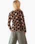 A woman viewed from behind wearing a long-sleeve top with a black and peach checkerboard pattern featuring small heart and star motifs, paired with light blue jeans against a plain white background.