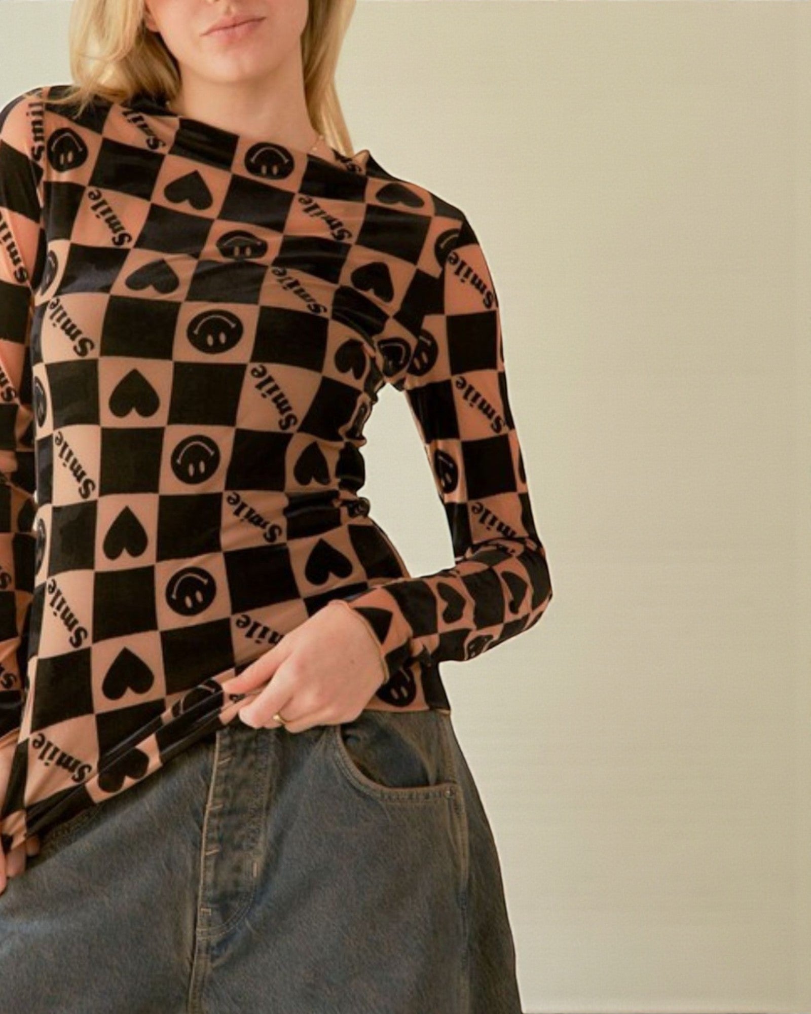 Person wearing a long-sleeve shirt with a pattern of hearts, squares, and text on a plain background