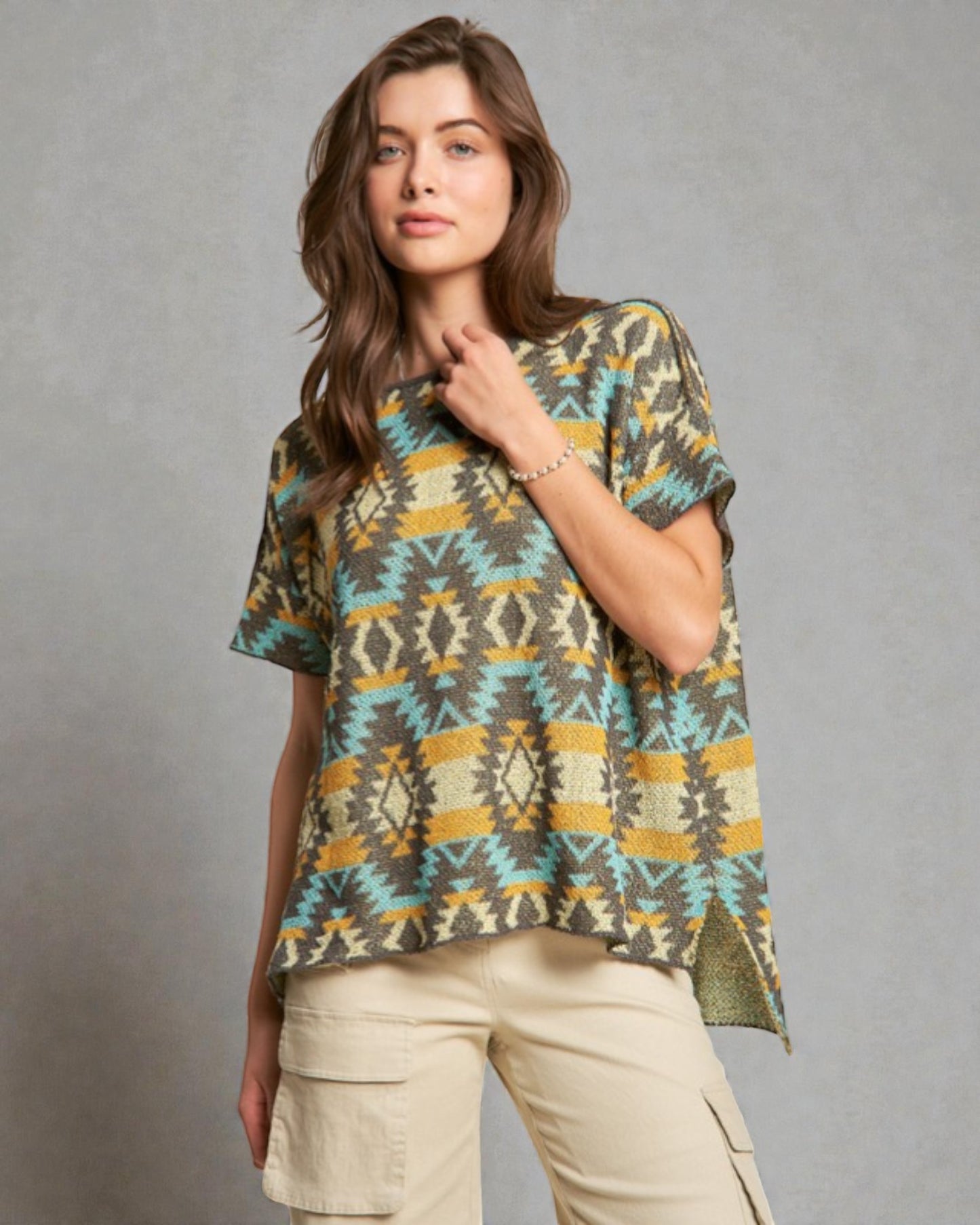 Woman wearing a patterned shirt and beige pants against a gray background
