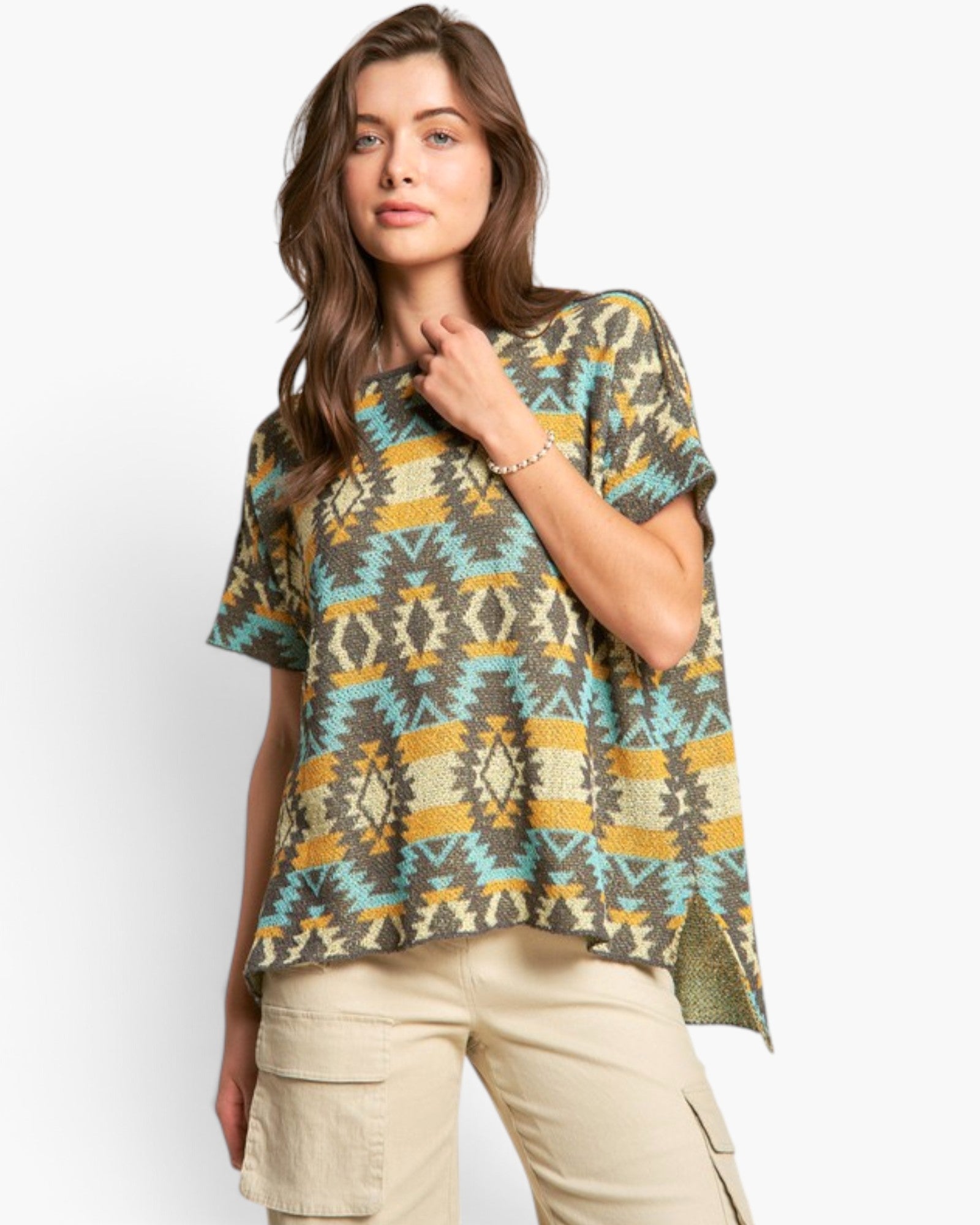 A woman modeling a short-sleeve knit top with a geometric Southwestern pattern in olive green, turquoise, mustard yellow, and beige, paired with khaki cargo pants against a light gray studio background.