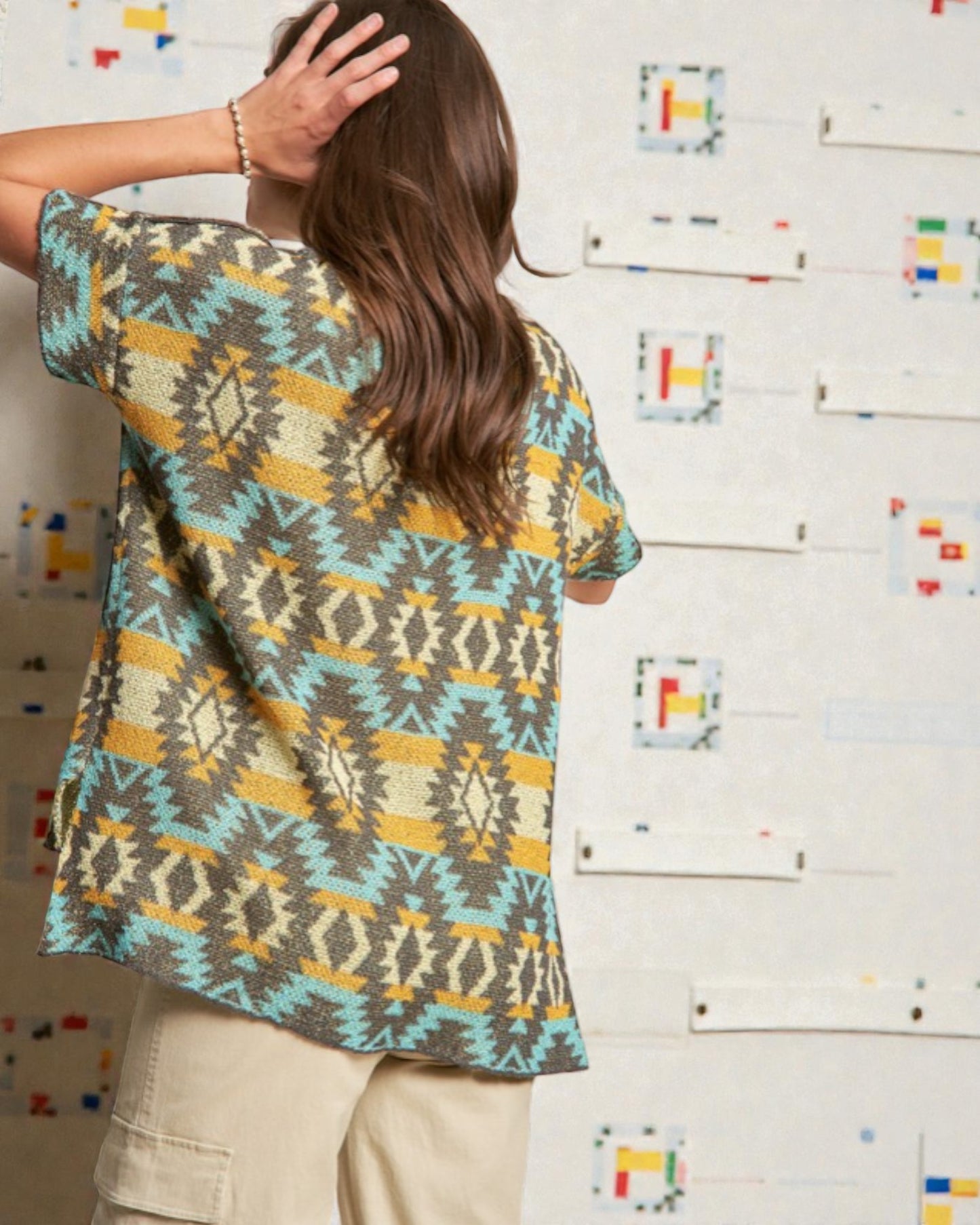 Person wearing a patterned shirt with a colorful abstract design on a wall.