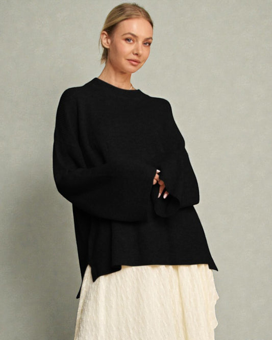 Woman wearing a black sweater and white pants against a plain background