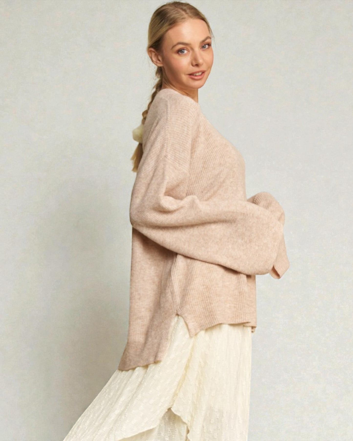 Woman wearing a beige sweater and white skirt against a plain background