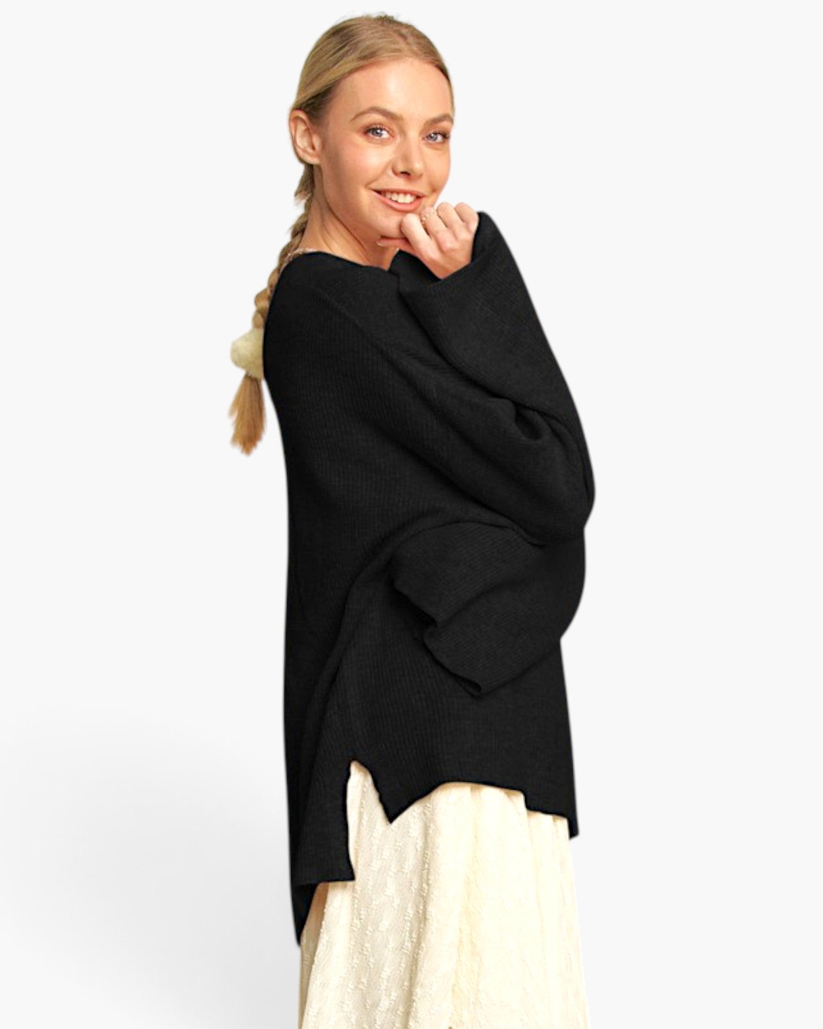 A woman modeling a black knit poncho-style sweater over a cream dress, photographed against a clean white studio background.