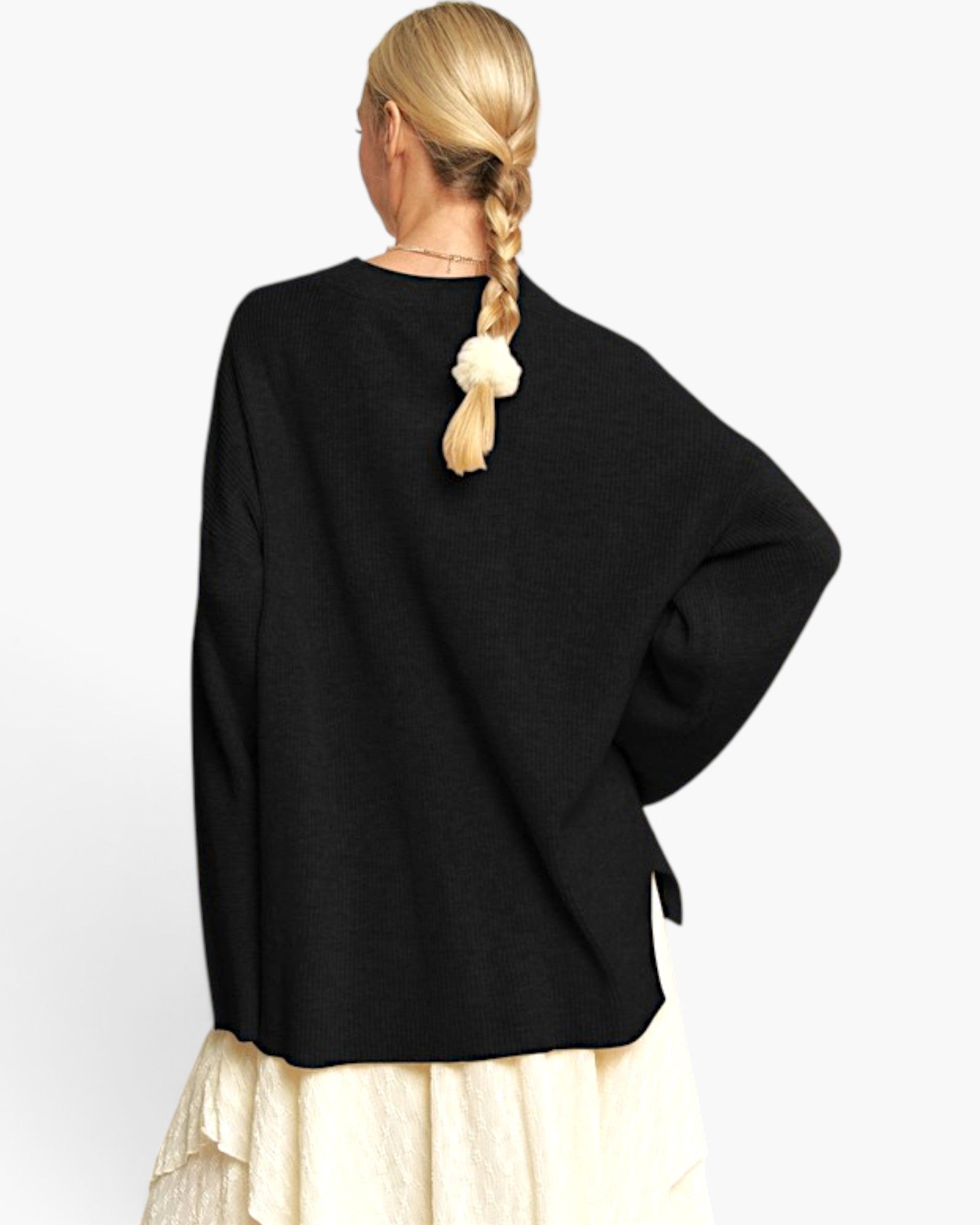 A woman shown from the back wearing a black oversized knit sweater with wide sleeves and a cream pleated skirt, against a plain light background.
