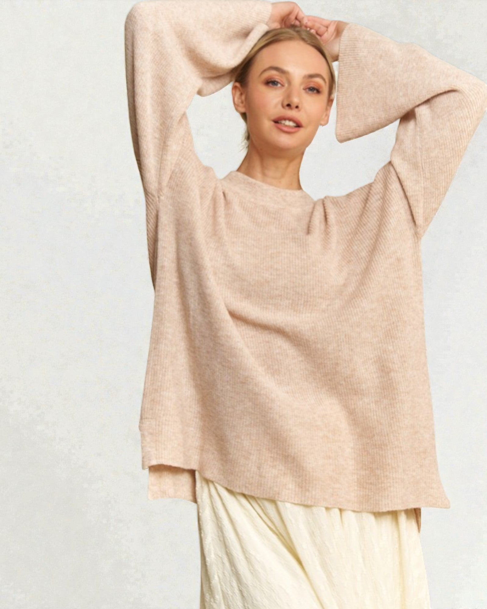 Woman wearing a beige sweater and white pants against a light gray background