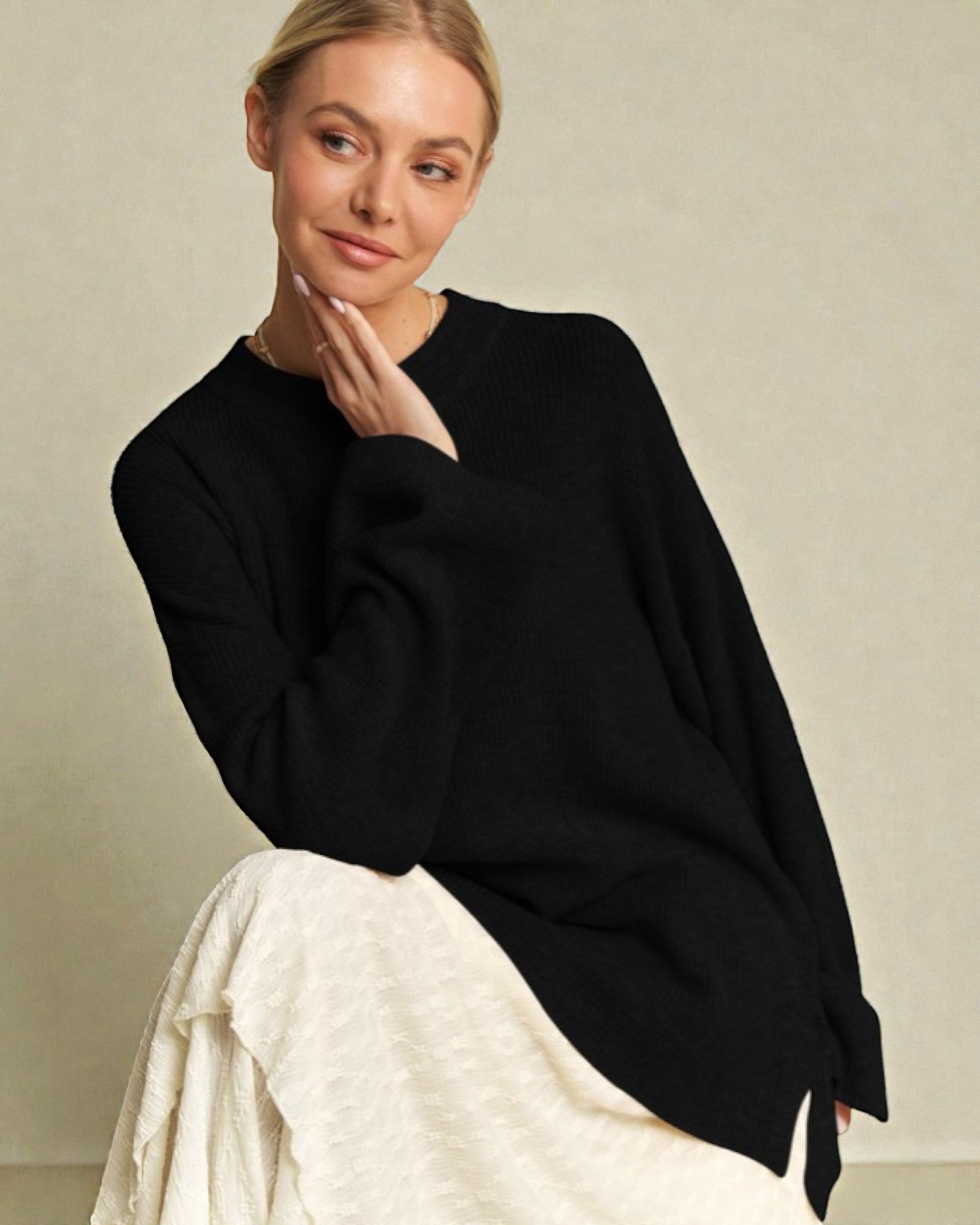 Woman wearing a black sweater and white pants against a beige background