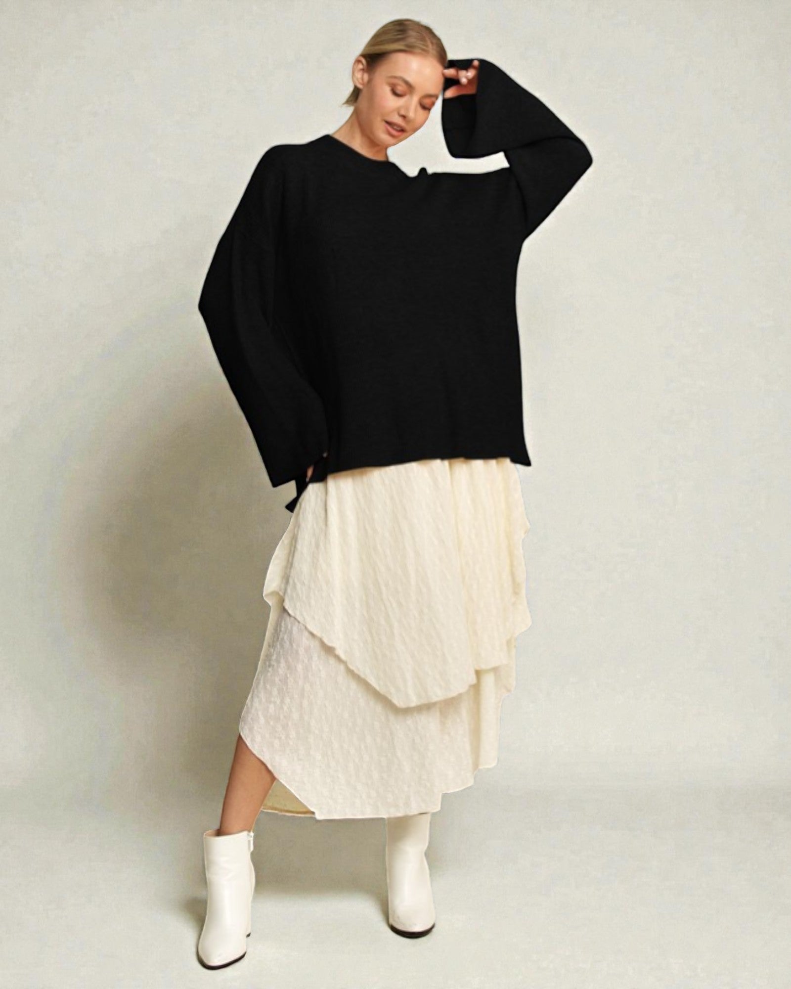 Woman wearing a black sweater and white skirt on a plain background