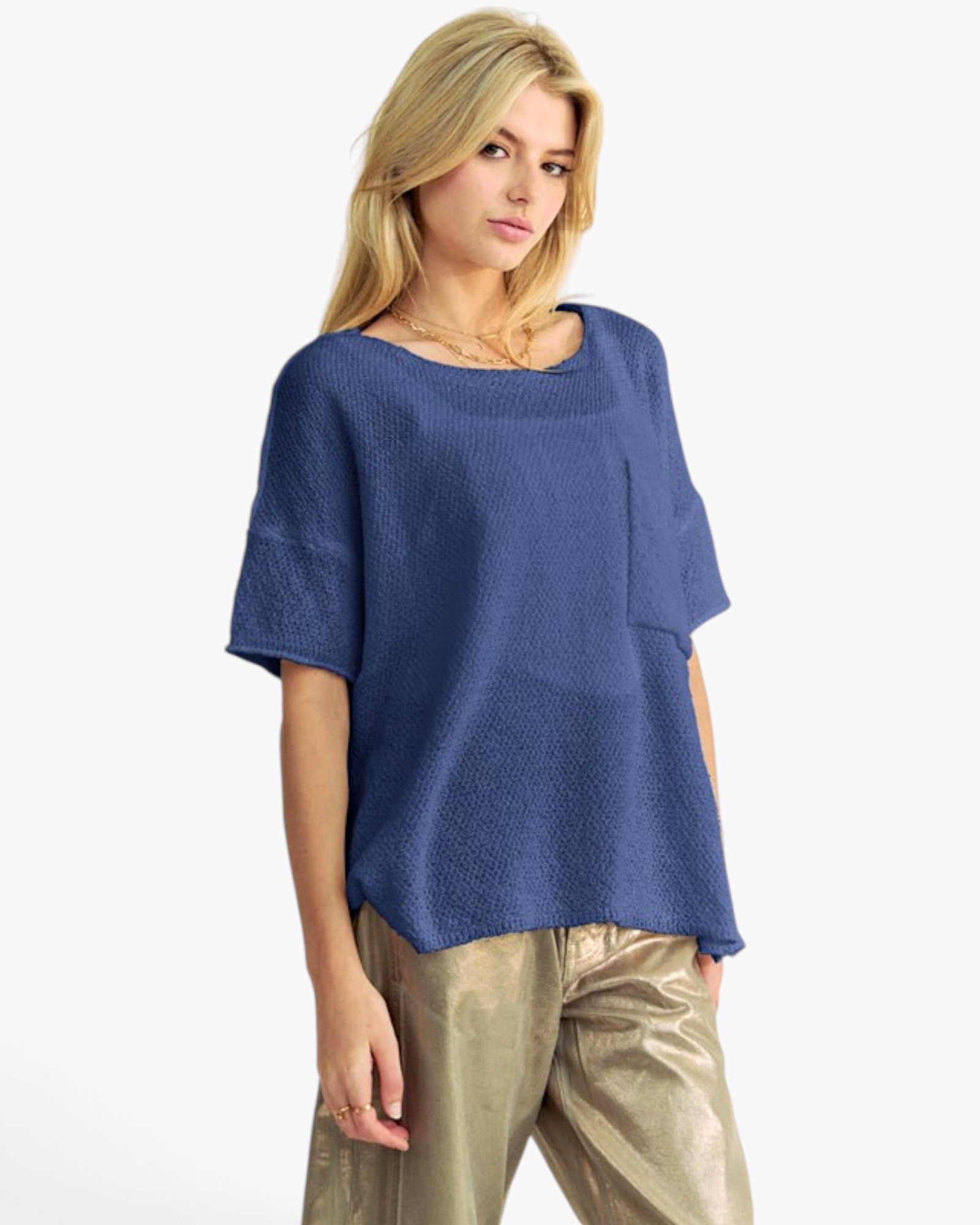 A blonde model wearing a textured, short-sleeved blue knit top and shiny metallic gold pants, photographed against a clean white background.