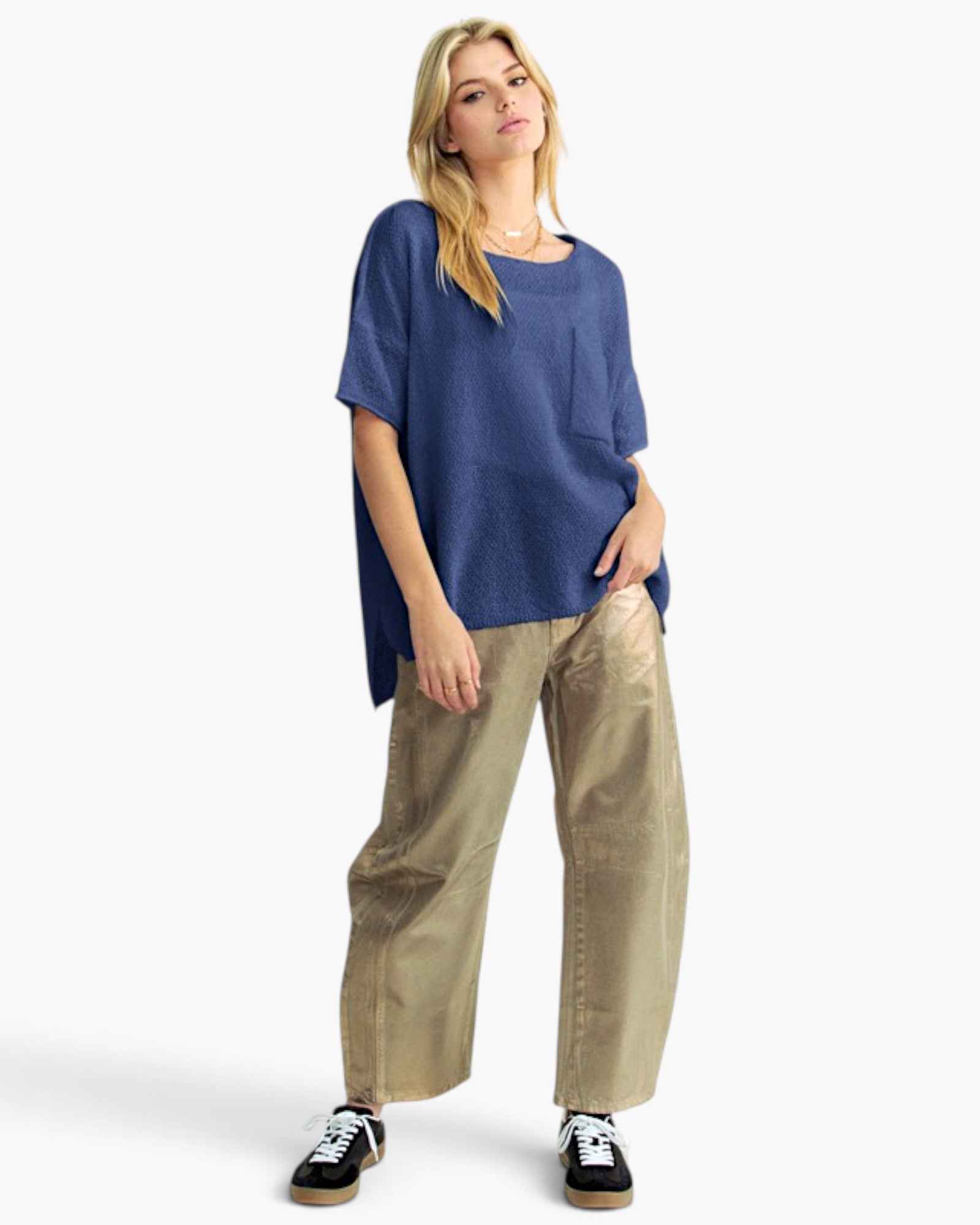 A woman modeling a loose-fitting heathered blue short-sleeve top, paired with wide-leg beige pants and black sneakers, against a clean white studio background.