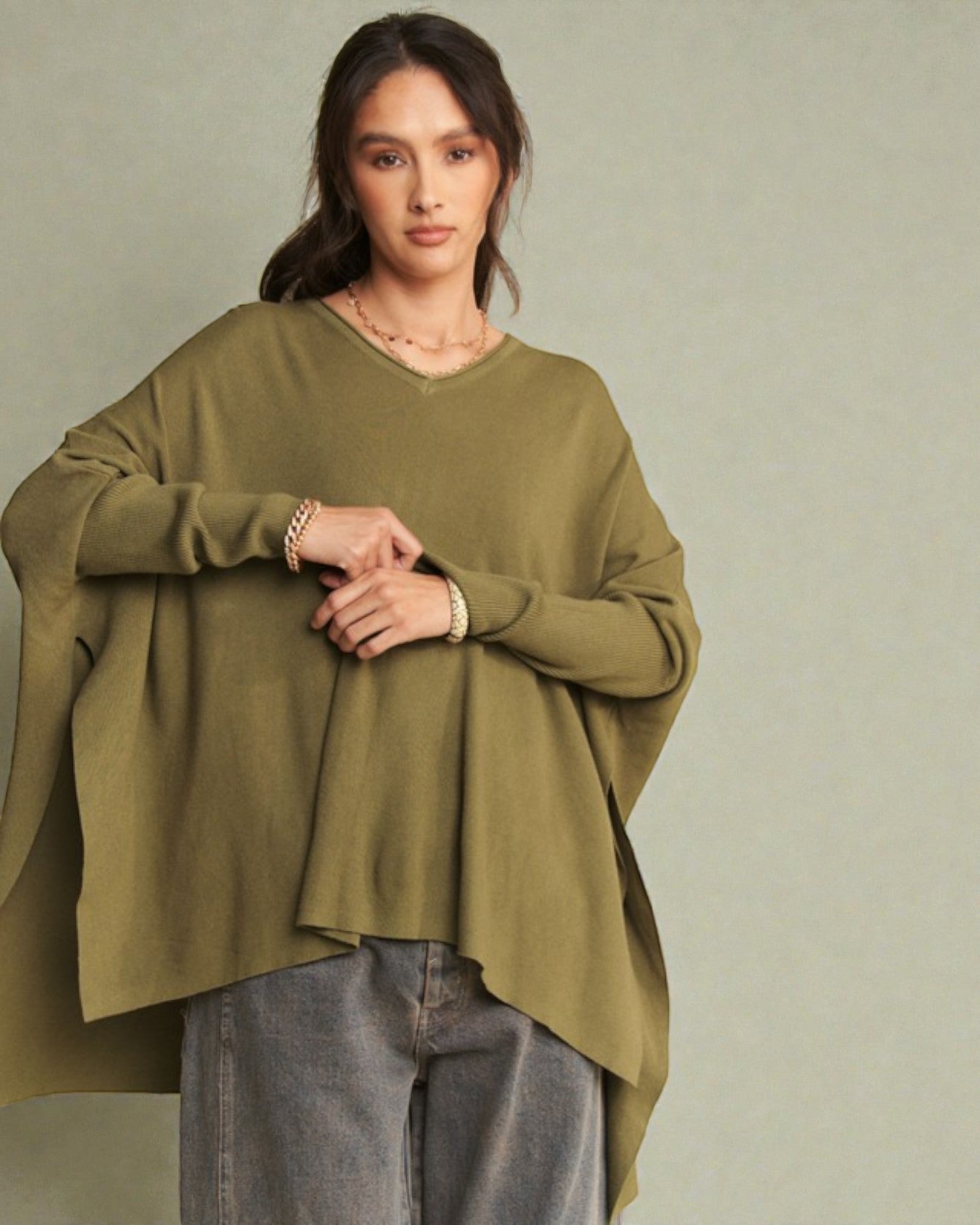 Woman wearing an olive green sweater and gray pants against a plain background