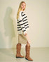 Woman wearing a black and white striped sweater and brown knee-high boots against a plain background