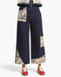 A person wearing dark navy wide-leg patchwork pants with beige floral print inserts, paired with red sneakers, shown from the waist down on a light gray studio background.