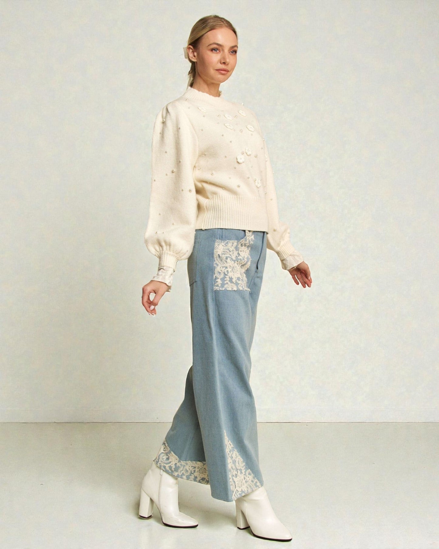 Woman wearing a cream blouse and light blue pants with floral embroidery on a plain background