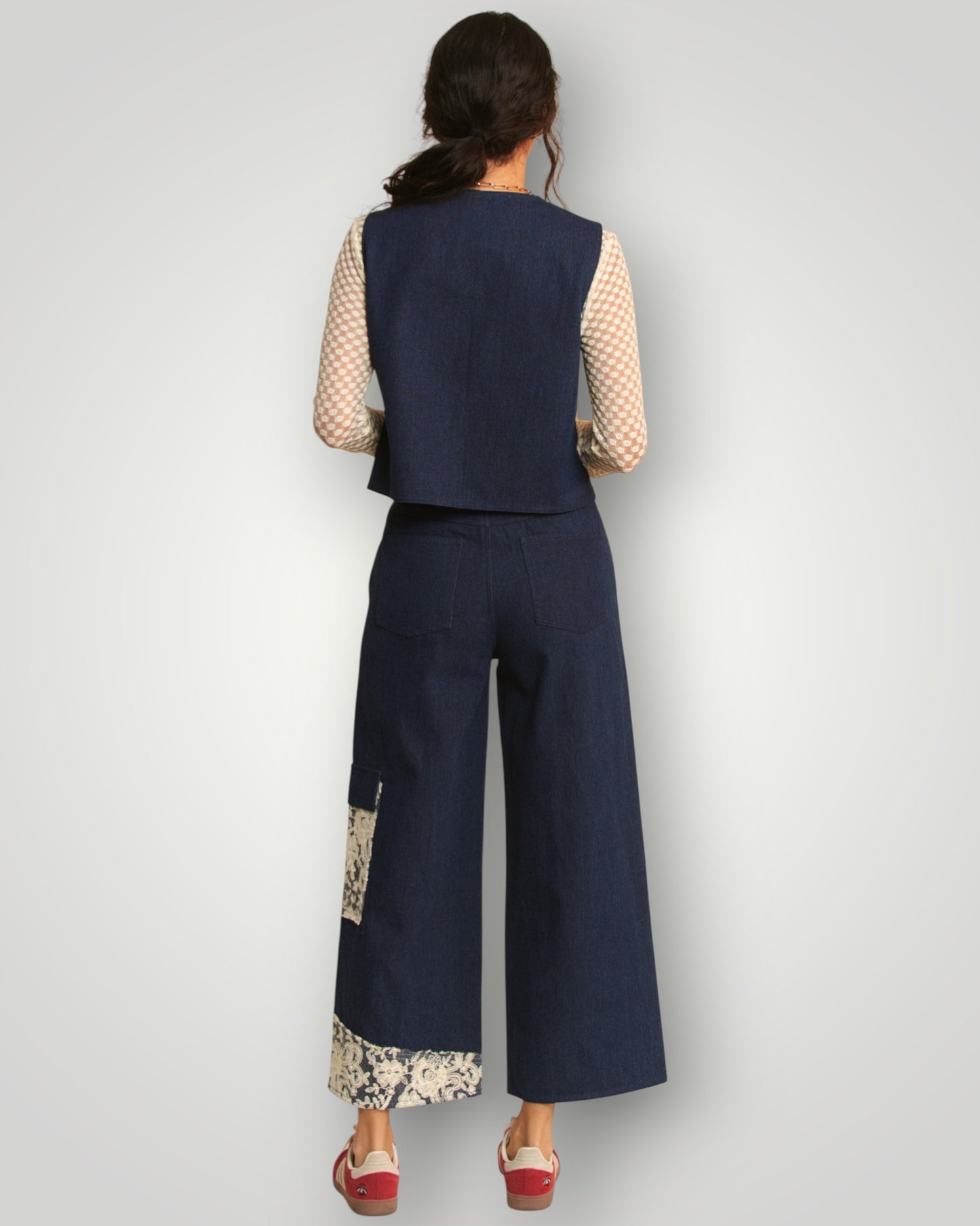 Person wearing a navy blue sleeveless top and wide-leg pants with floral details on a light gray background