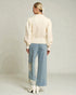 Woman wearing a cream blouse and light blue pants with lace details on a plain background