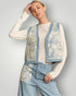 Woman wearing a stylish outfit with a floral patterned top and blue pants against a plain background