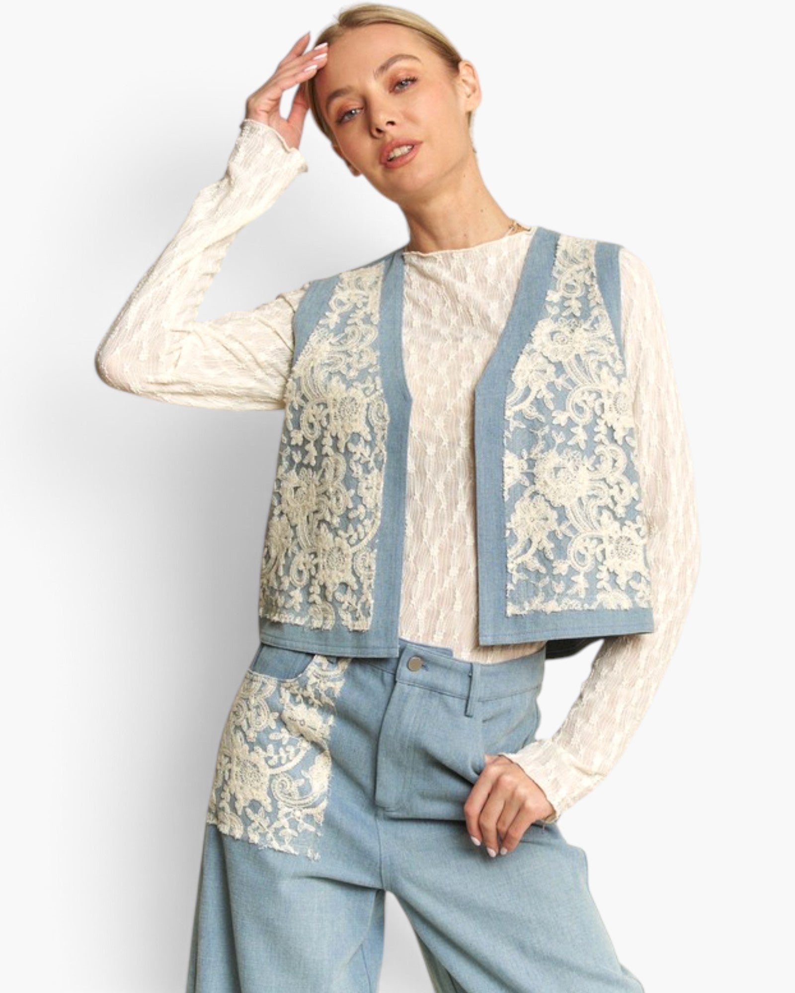 A model wearing a light blue denim vest with cream lace panels over a cream patterned long-sleeve top and matching light blue denim trousers, set against a plain white studio background.