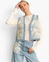 A model wearing a light blue denim vest with cream lace panels over a cream patterned long-sleeve top and matching light blue denim trousers, set against a plain white studio background.