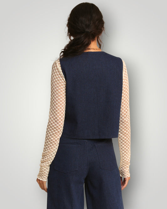 Person wearing a navy vest over a beige patterned shirt with a plain background