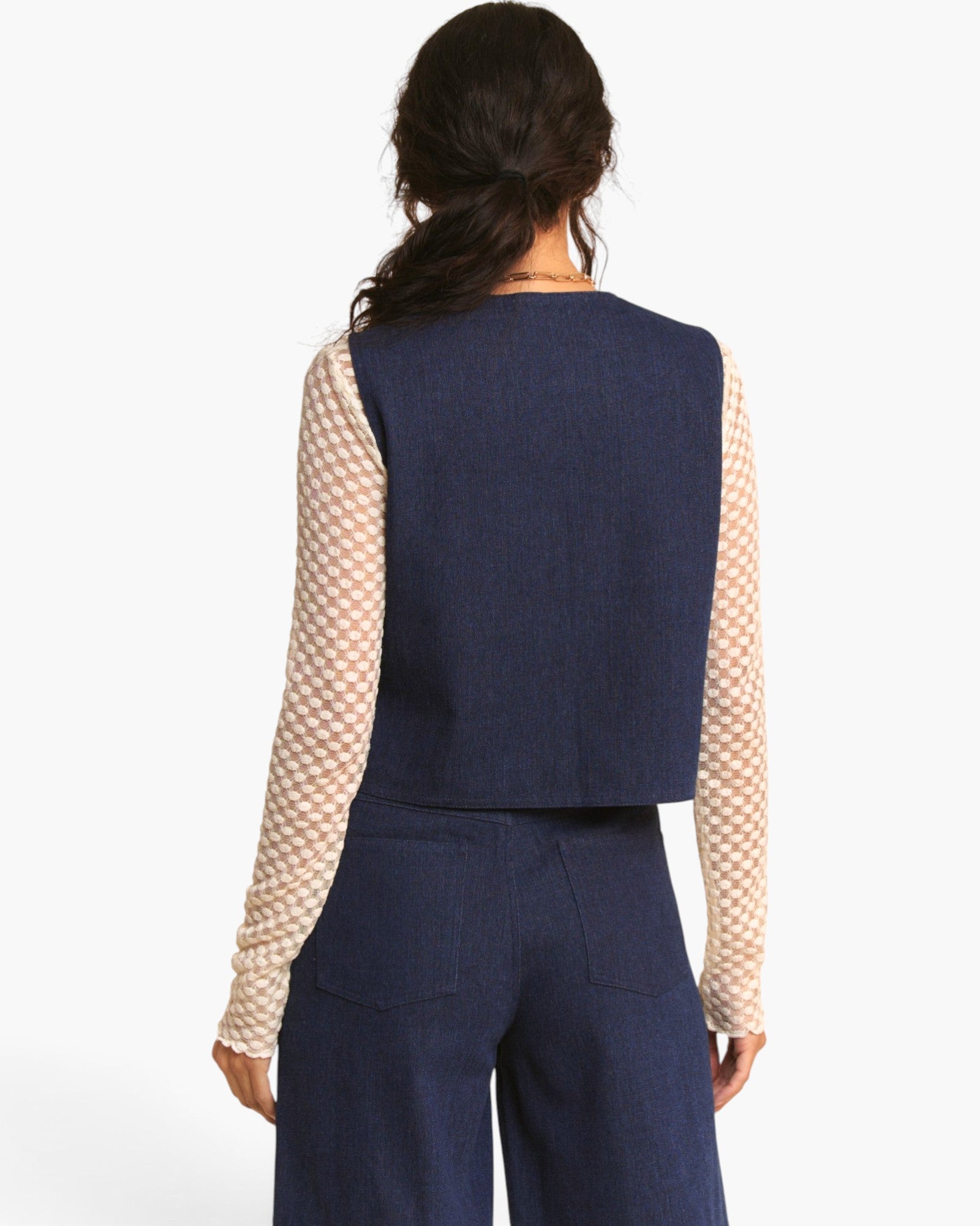 A model shown from the back wearing a navy blue sleeveless vest over a beige and white patterned long-sleeve top, paired with navy blue wide-leg trousers, against a plain white background.