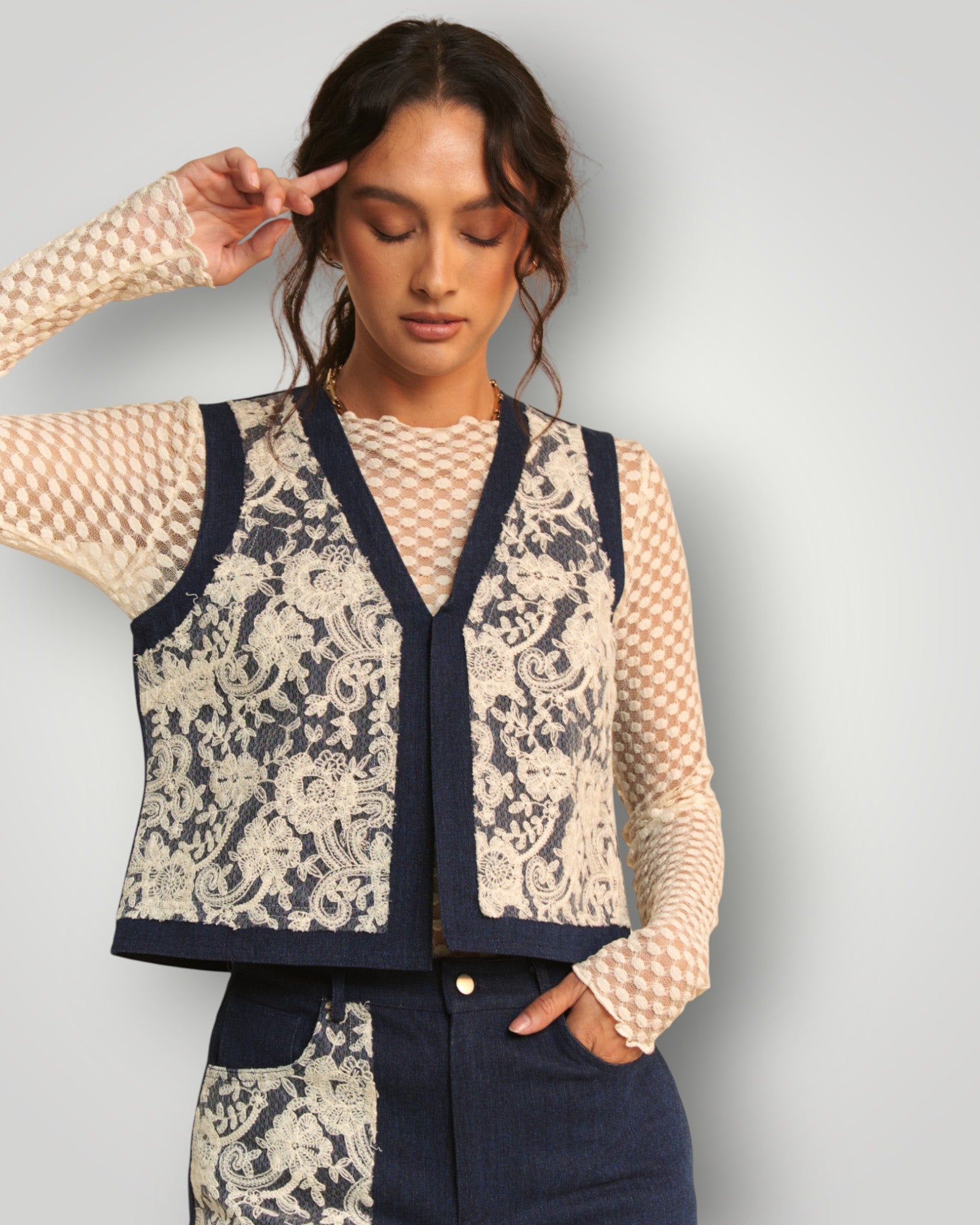 Woman wearing a patterned vest over a sheer top with a plain background